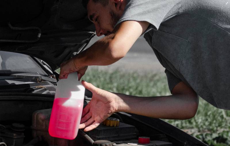 A man pours bright pink coolant into the coolant reservoir of a car