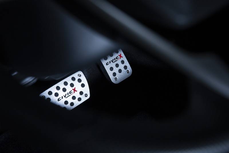 A moody photo of a brake pedal and an accelarator pedal in the footwell of a Honda Civic X car